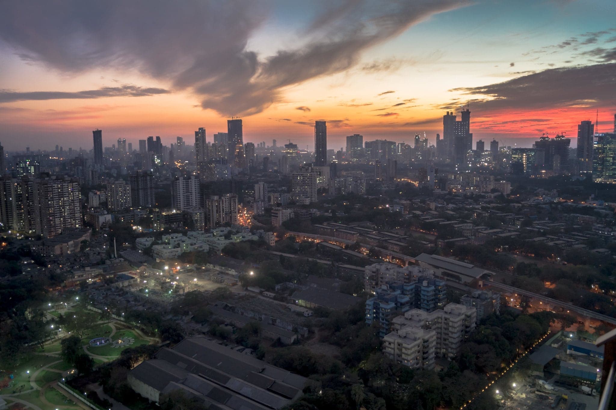 A city skyline at dusk, with streets and towers lighting up under a dramatic sky
