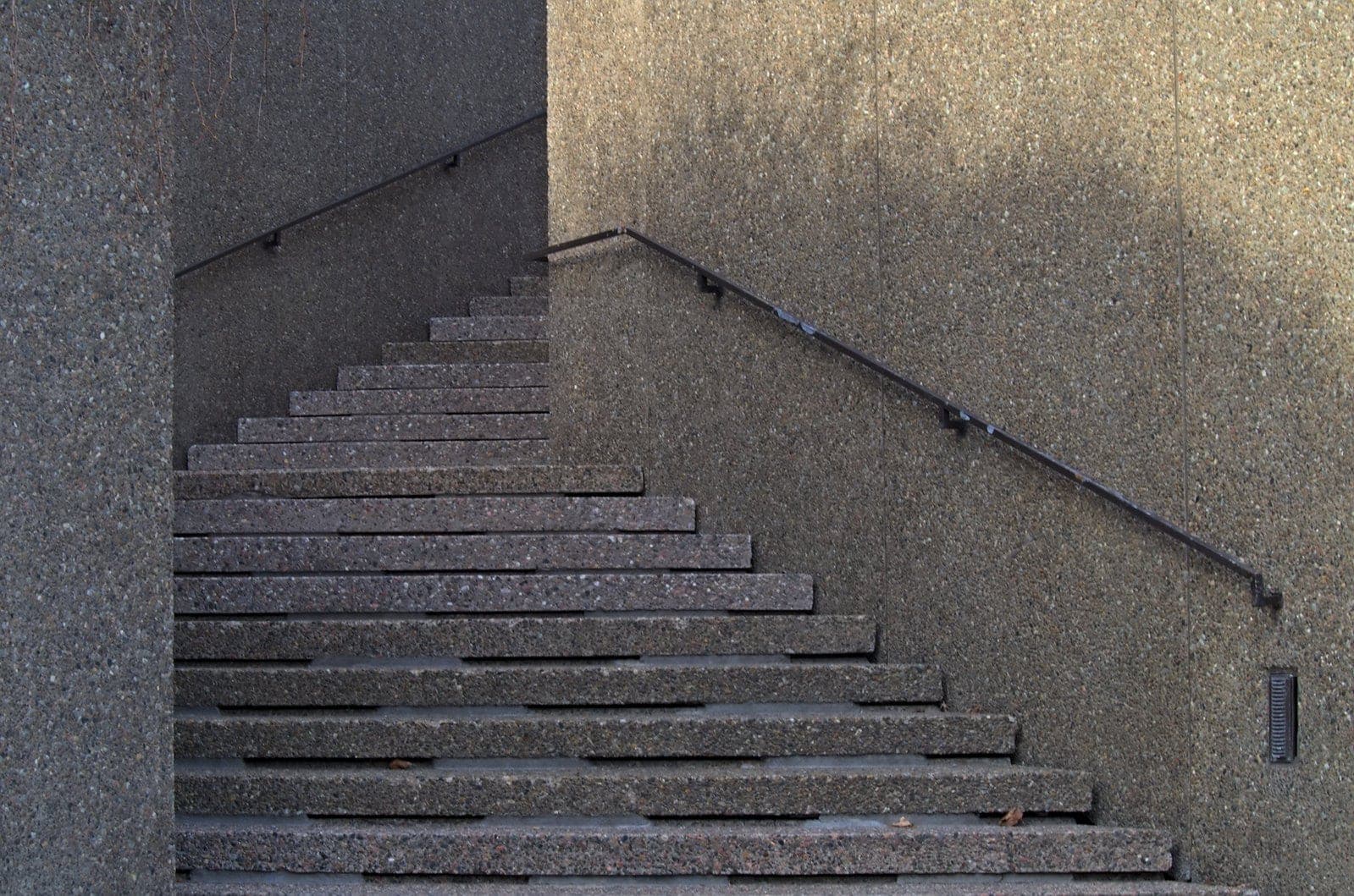 A concrete stairway with a handrail rising through a quiet stone building
