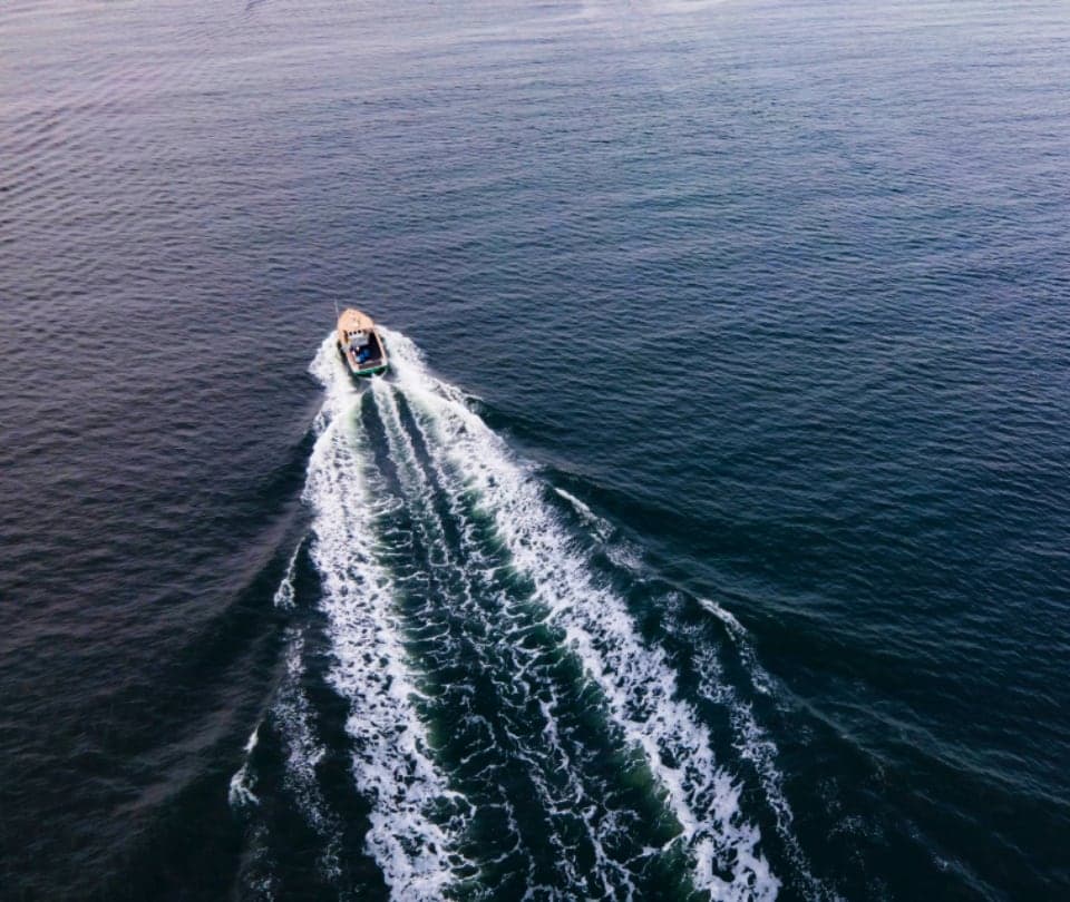 Aerial view of a boat leaving a white wake across dark water